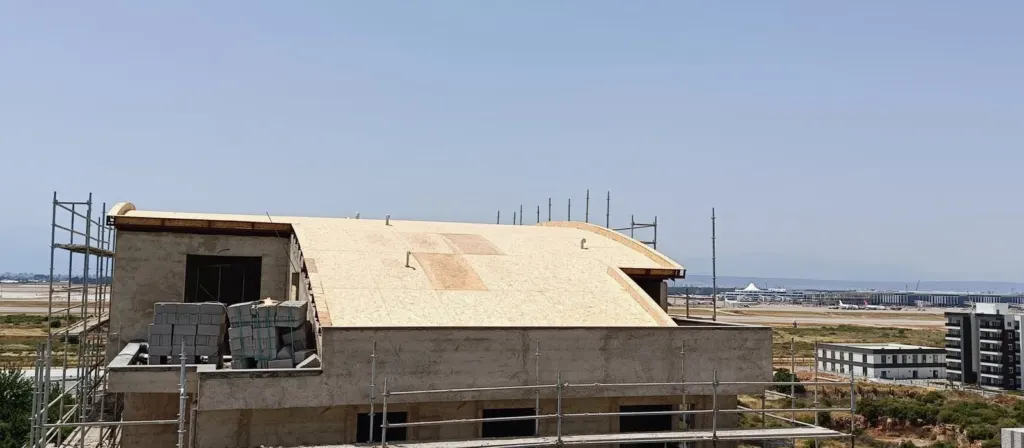 Eğimli çatı yüzeyi ahşap levhalarla kaplanmış, kenarında iskele duruyor