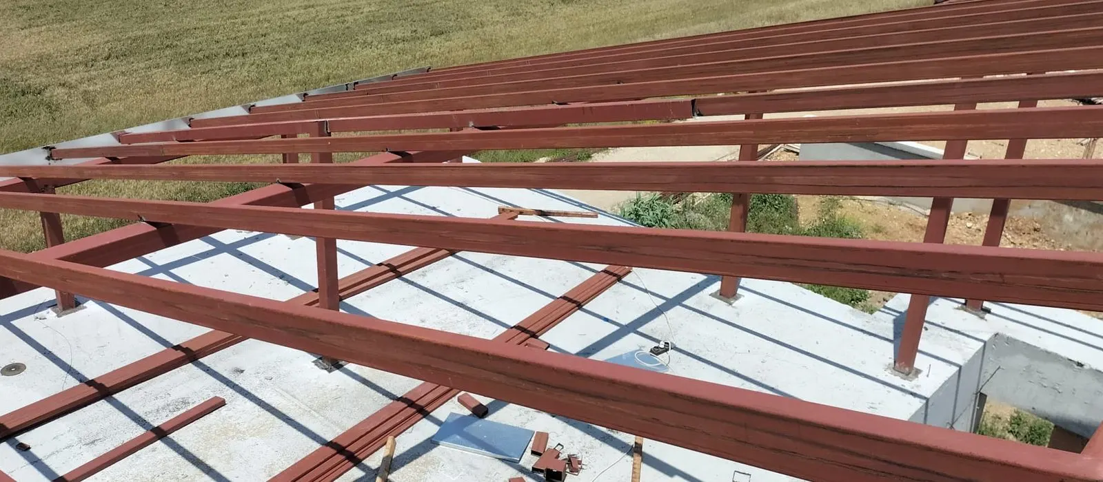 Beton döşeme boyunca uzanan çelik aşıklar, arkada açık tarla görünüyor