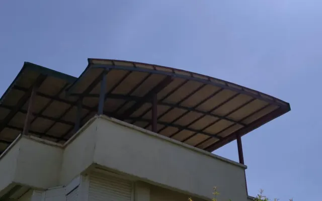 Terasın üzerine kurulmuş kavisli metal örtü, alttan ve güneşe karşı görünüyor