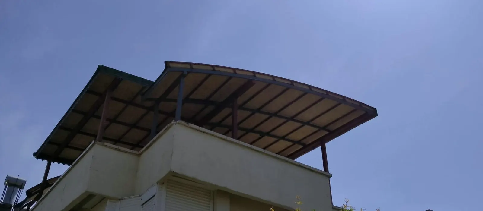 Terasın üzerine kurulmuş kavisli metal örtü, alttan ve güneşe karşı görünüyor